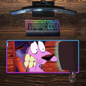 May include: A computer setup featuring a curved monitor, a rainbow-lit keyboard, and a mouse pad with a cartoon image of Courage the Cowardly Dog. A decorative mouse is also present.