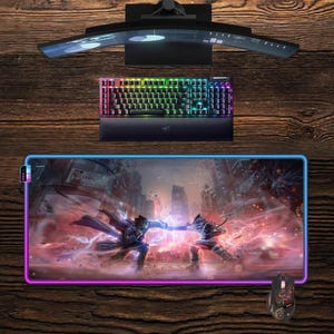 Può includere: Un monitor per computer curvo, una tastiera retroilluminata e un mouse da gioco sono esposti su una superficie di legno. La tastiera ha tasti color arcobaleno. È presente anche un ampio tappetino per mouse con una grafica colorata di due figure che combattono.