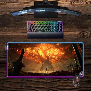 May include: A gaming setup featuring a curved monitor, a backlit keyboard, a mouse, and a large mousepad with a fantasy scene. The mousepad has a colorful border. The keyboard and mouse have RGB lighting.