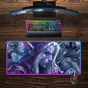 Op de afbeelding: Een gaming-opstelling met een gebogen monitor, een toetsenbord met achtergrondverlichting en een muis. Een grote muismat toont een fantasiekarakter met een wolf, omlijst door een oplichtende paarse en blauwe rand. Het toetsenbord heeft veelkleurige toetsen.
