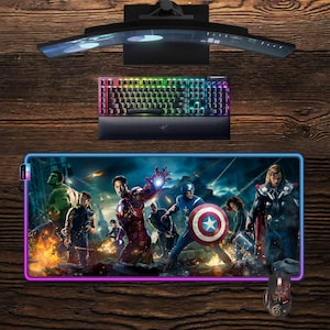 May include: A gaming setup featuring a curved monitor, a backlit keyboard, and a large mousepad with an Avengers graphic. A matching mouse is also visible. The setup is on a wooden surface.
