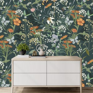 May include: A white dresser with four drawers and a light wood top. The background is a dark green floral wallpaper with orange flowers, white flowers, butterflies, and greenery. A small potted plant and decorative items sit on top of the dresser.
