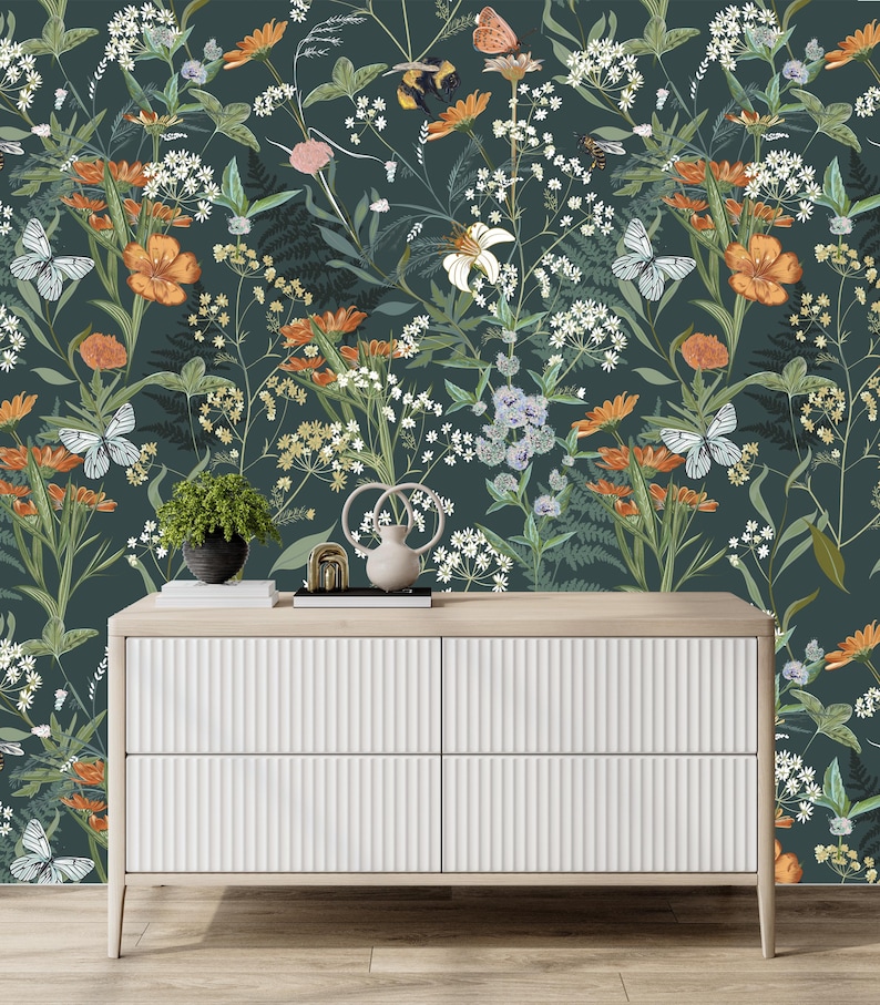 May include: A white dresser with four drawers and a light wood top. The background is a dark green floral wallpaper with orange flowers, white flowers, butterflies, and greenery. A small potted plant and decorative items sit on top of the dresser.