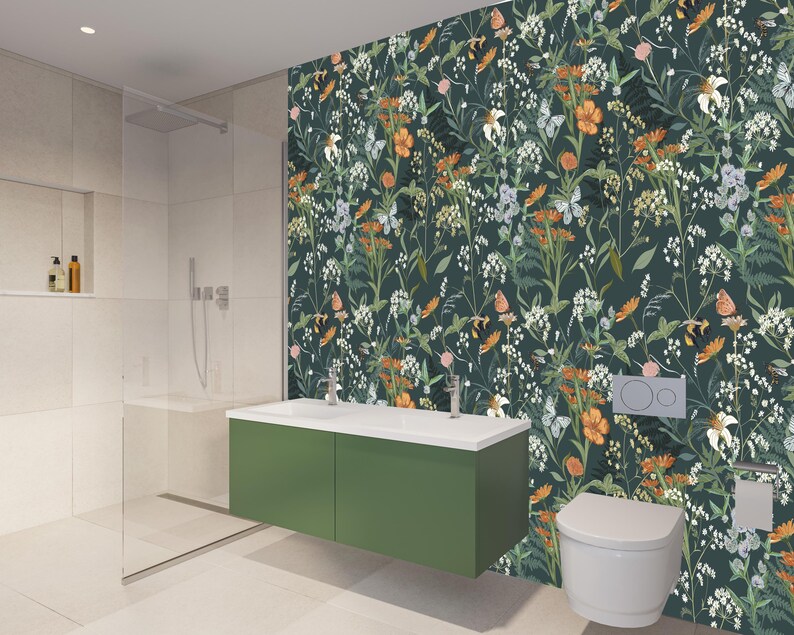 May include: A modern bathroom with a green vanity, white sink, and toilet. The wall features a dark green floral wallpaper with orange, white, and purple flowers. A glass shower enclosure is on the left.