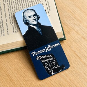 May include: A rectangular bookmark featuring a portrait of Thomas Jefferson against a light blue background. The lower section is dark blue with the text Thomas Jefferson and a graphic illustration of the Declaration of Independence document.