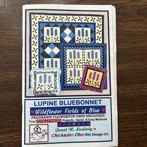 May include: A printed pattern for quilting projects, featuring the text "Lupine Bluebonnet" and "Wildflower Fields of Blue." The design includes various blue and purple floral quilt blocks. The pattern is from Chickadee Charms Design Co.