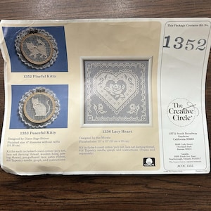 May include: A package featuring three cross-stitch kits. Two kits are labeled "Playful Kitty" and "Peaceful Kitty", each with a cat design. The third kit is "Lacy Heart", with a heart and rose design. The package includes kit number 1352.