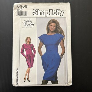 以下が含まれることがあります： クリスティ・ブリンクリーコレクションのSimplicityソーイングパターン。パッケージには、青とピンクの2つのドレスのイラストが描かれています。パターンにはサイズ8とSimplicityのブランド名が記載されています。