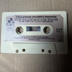 May include: A beige cassette tape titled Disney presents CHILDREN'S FAVORITES, Side 2. The label features a Mickey Mouse illustration and a tracklist including Oh, Susanna, Billy Boy, and Home on the Range. Copyright 1987 The Walt Disney Company.