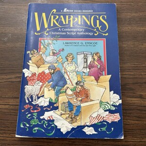 May include: A blue book titled "WRAPPINGS" with the subtitle "A Contemporary Christmas Script Anthology." The cover features illustrations of people in boxes with Christmas decorations. The author's name is Lawrence G. Enscoe.