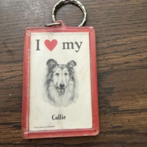 May include: A rectangular keychain with a red plastic frame and a metal ring. The insert features a black and white sketch of a Collie dog, the text I heart my Collie, and the small printed text 1981 STRAND ENTERPRISES at the bottom.