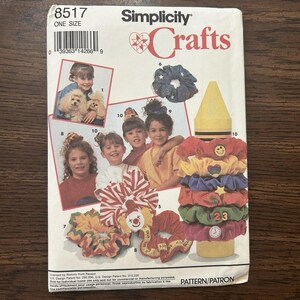 May include: Simplicity Crafts pattern for making scrunchies. The pattern features images of children and various scrunchie designs, including those with smiley faces, hearts, stars, and numbers. The pattern is labeled "One Size".