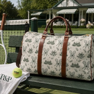 Könnte beinhalten: Eine Reisetasche aus cremefarbenem Stoff mit einem sich wiederholenden dunkelgrünen Druck von Tennisschlägern und Clubhausgebäuden, akzentuiert durch braune Ledergriffe und Besätze. Ein weißes Handtuch mit den Buchstaben P&P, ein Tennisball und eine Trinkflasche.
