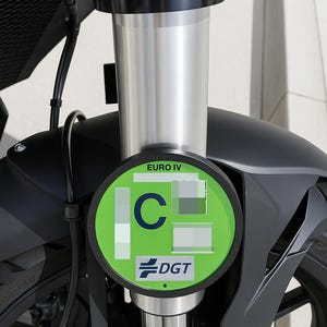 Puede incluir: Primer plano de la suspensión delantera de una motocicleta, con horquilla plateada y guardabarros negro. Una pegatina circular verde con la letra "C" y el texto "EURO IV" y "DGT" está adherida a la horquilla.