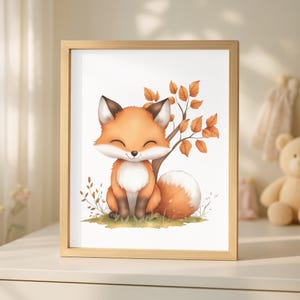 Op de afbeelding: Een ingelijste prent met een lachende cartoonvos met oranje en witte vacht, zittend bij een boom met oranje bladeren. Het kunstwerk staat tegen een witte achtergrond, omlijst door een licht houten frame. Thema: herfstbos.