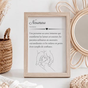 Peut inclure: Un cadre en bois clair contenant une impression avec le mot Nounou, sa définition, et un dessin au trait noir représentant une main d'adulte tenant la main d'un enfant avec un cœur au centre, le tout sur un fond blanc.