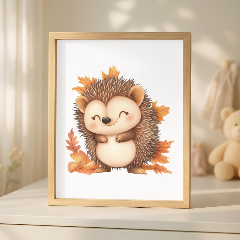 Op de afbeelding: Een ingelijste prent met een vrolijke cartoonegel met een lichtbruin lichaam, omringd door herfstbladeren. De egel heeft een lachend gezicht en staat tegen een witte achtergrond. De lijst is gemaakt van lichtgekleurd hout.