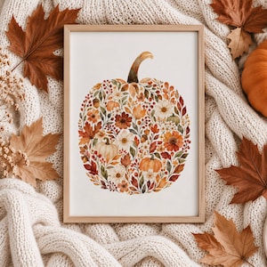 Peut inclure: Un cadre en bois rectangulaire contenant une impression sur fond blanc représentant une citrouille composée de divers éléments botaniques automnaux, incluant des feuilles orange, rouges et brunes, des baies et des fleurs aux tons chauds.