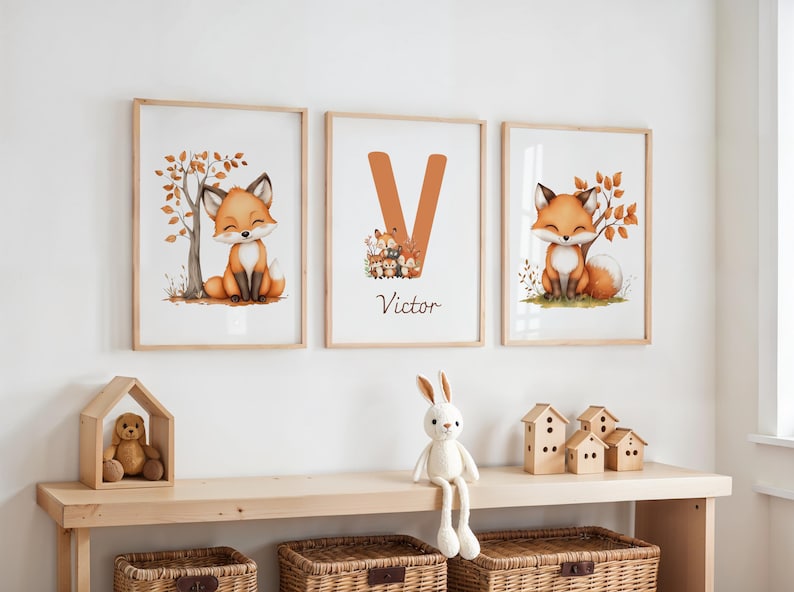 Op de afbeelding: Drie ingelijste aquarelprints met een schattige vos met oranje en bruine vacht. De prints zitten in houten frames en bevatten een boom, de letter "V" met de naam "Victor" en een vos met herfstbladeren. Een houten plank bevat een teddybeer, een konijn en houten huisjes.
