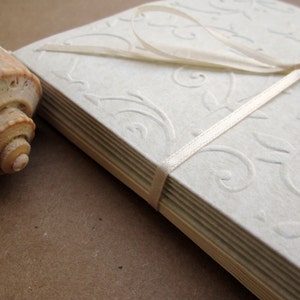 May include: A stack of white paper cards with a delicate embossed floral pattern. The cards are tied together with a white satin ribbon.