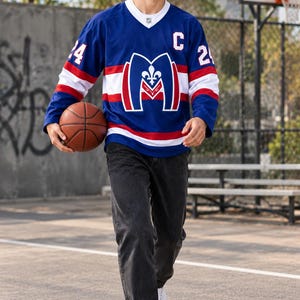 May include: A blue, white, and red hockey jersey featuring a large letter M logo with a fleur-de-lis, the letter C on the chest, and the number 24 on the sleeves, paired with black denim jeans and white sneakers while holding a basketball.