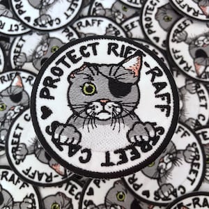 May include: Embroidered patch with a gray cat wearing an eye patch. The cat is surrounded by the words "PROTECT STREET CATS RAFF" in a circular design. The patch has a black border and is on a white background.