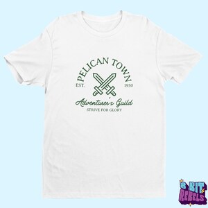 K&ouml;nnte beinhalten: Wei&szlig;es T-Shirt mit einem gr&uuml;nen Aufdruck. Das Design zeigt die Worte "PELICAN TOWN", gekreuzte Schwerter und "Adventurer's Guild". Das T-Shirt hat auch den Text "EST. 1950" und "STRIVE FOR GLORY".
