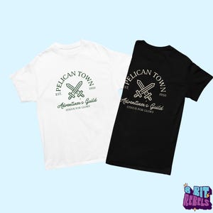 K&ouml;nnte beinhalten: Zwei T-Shirts, eines wei&szlig; und eines schwarz, mit einem kreisf&ouml;rmigen Grafikdesign. Das Design enth&auml;lt den Text "PELICAN TOWN" &uuml;ber gekreuzten Schwertern, mit "EST. 1950" und "Adventurer's Guild STRIVE FOR GLORY" darunter. Die Shirts sind vor hellblauem Hintergrund.