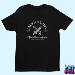 K&ouml;nnte beinhalten: Schwarzes T-Shirt mit wei&szlig;em Aufdruck. Das Design zeigt den Text "PELICAN TOWN", gekreuzte Schwerter und "Adventurer's Guild". Das Shirt hat auch den Text "EST. 1950" und "STRIVE FOR GLORY".