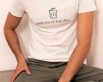 Peut inclure: T-shirt blanc à col rond avec un dessin noir d'une poubelle et le texte "sudo rm -rf / bad vibes". La personne porte un pantalon vert olive et des baskets noires.