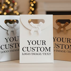 Può includere: Tre sacchetti regalo personalizzati in argento, bianco e beige. Ogni sacchetto ha un manico, un fiocco e le parole "YOUR CUSTOM LOGO/IMAGE/TEXT" stampate in nero. I sacchetti sono su una superficie chiara.