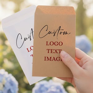 May include: Two custom envelopes, one white and one kraft brown, are held in a hand. The brown envelope displays the words "Custom", "LOGO", "TEXT", and "IMAGE" in a red font. The white envelope has the word "Custom" in black.