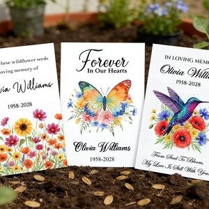 May include: Three memorial seed packets with floral and butterfly designs. The packets read "Scatter these wildflower seeds in loving memory of Olivia Williams 1958-2028", "Forever In Our Hearts Olivia Williams 1958-2028", and "In Loving Memory Olivia Williams 1958-2028".