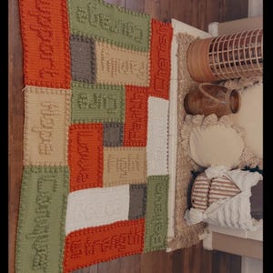 May include: A colorful, textured crochet rug with various rectangular patches in orange, green, beige, white, and gray. Each patch features a word like "Hope" or "Courage" in raised lettering. The date "Feb 14, 2026" is also visible.