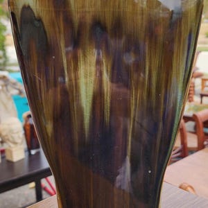 May include: A tall, glazed ceramic vase with a flared shape. The vase features a blend of brown, green, and black vertical streaks, creating a unique, textured appearance. The vase is a decorative item.
