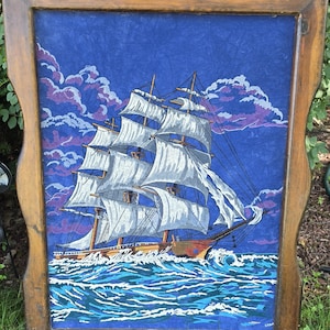 May include: A rectangular wooden frame containing a painting of a large sailing ship with white sails on a dark blue sea. The sky is filled with purple and blue clouds. The ship is depicted in motion, cutting through waves with white foam.