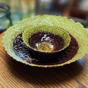 May include: Set of three decorative glass bowls in varying sizes. The largest bowl is a light green with a textured, ruffled edge. The middle bowl is a deep brown with a textured surface, and the smallest bowl is a golden yellow.
