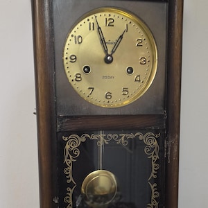 May include: A vintage wooden wall clock with a gold-colored face and hands. The clock face has black numerals and the word "Centurion" at the top. The clock has a pendulum and a decorative glass panel below the clock face.