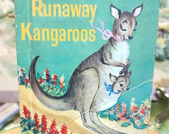 May include: Vintage children's book titled "The Runaway Kangaroos." The cover features an illustration of a kangaroo with a joey in its pouch, set against a teal background with red and yellow flowers. The book is a Rand McNally Junior Elf Book.