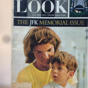 May include: A vintage magazine cover featuring a photograph of a woman and a child. The magazine is titled "LOOK" with the text "THE JFK MEMORIAL ISSUE." The cover has a color palette of yellow, black, white, and gray.