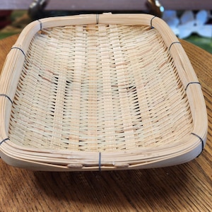 May include: A rectangular bamboo basket with a woven design. The basket has rounded corners and is held together with black string. The natural bamboo color is visible throughout the basket.