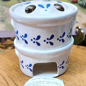 May include: A two-piece, off-white ceramic potpourri pot with blue floral designs. The top section has a lid with air holes, and the bottom section has an opening for a candle. The pot is food safe and dishwasher safe.