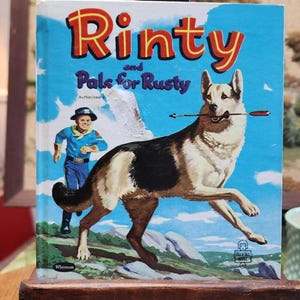 May include: Vintage children's book cover titled "Rinty and Pals for Rusty." The cover features a German Shepherd with an arrow in its mouth, a boy in a blue outfit, and the text "Rinty" in red and yellow. The background is a blue sky with clouds.