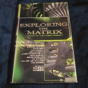 May include: A paperback book titled "Exploring the Matrix: Visions of the Cyber Present." The cover features a dark background with green and silver accents, and the title is in large, bold letters. The book includes writings on cyberpunk and cybernetic realities.