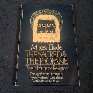 May include: A paperback book titled The Sacred & The Profane: The Nature of Religion by Mircea Eliade. The cover is black with gold text and a gold illustration of a stylized face. It includes the subtitle: The significance of religious myth, symbolism, and ritual within life and culture.