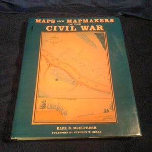 May include: A hardcover book titled "MAPS AND MAPMAKERS OF THE CIVIL WAR." The cover is teal with a central illustration of a detailed map in shades of orange and blue. The author's name, Earl B. McElfresh, and the foreword by Stephen W. Sears are also visible.