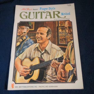 May include: A Mel Bay's basic Finger Style GUITAR Method instructional book featuring a cover illustration of three people playing acoustic guitars and a violin. The text includes the title, authors Hank Mackie and Phil Palermo, and publisher.