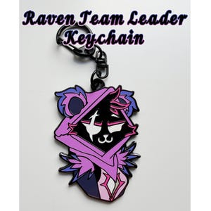 Peut inclure: Un porte-clés avec un design de personnage stylisé en noir, blanc et violet. Le porte-clés a un anneau en métal noir et un fermoir mousqueton. Le texte "Raven Team Leader Keychain" est au-dessus du personnage.