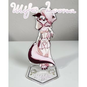 May include: A clear acrylic stand-up figure featuring a cartoon character with a white and maroon color scheme. The figure has a stylized design with the text "Wife Loona" in cursive script at the top. The base is a clear, hexagonal shape with floral accents.