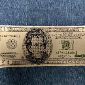 Puede incluir: Un parche bordado blanco y verde de un billete de veinte dólares con un retrato de Andrew Jackson. El parche tiene el texto "Twenty" y "United States of America" impreso en él.